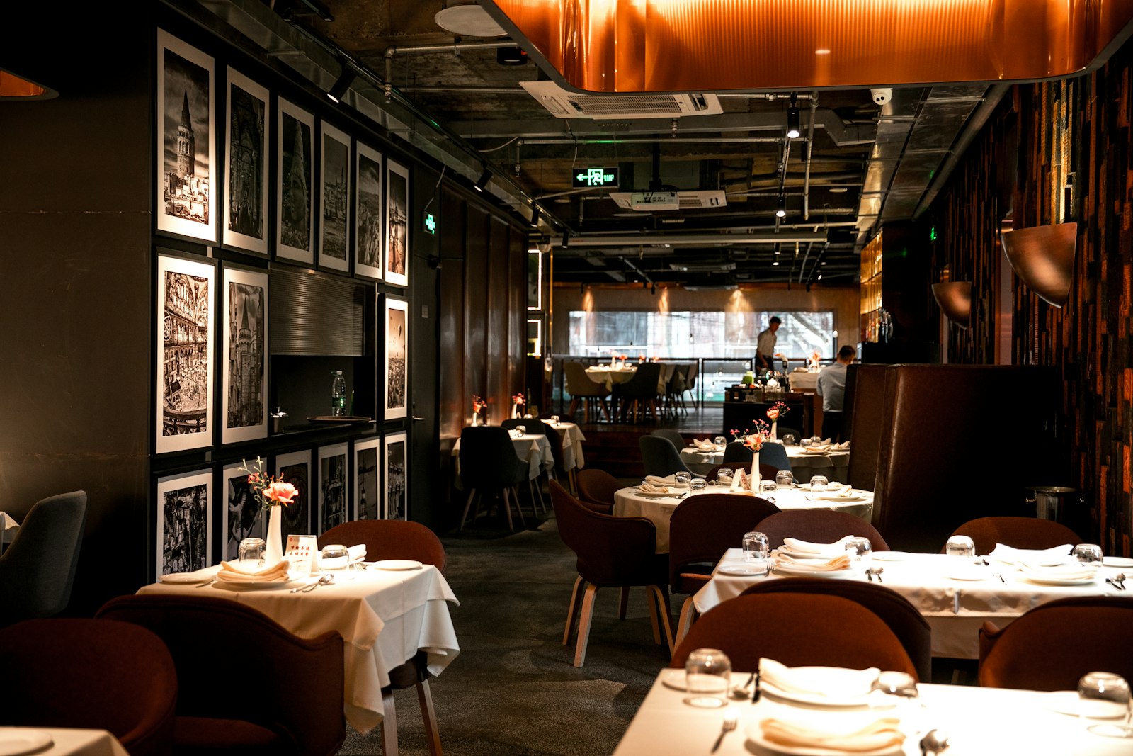 A dining room of set tables under warm light, framed photographs along one wall